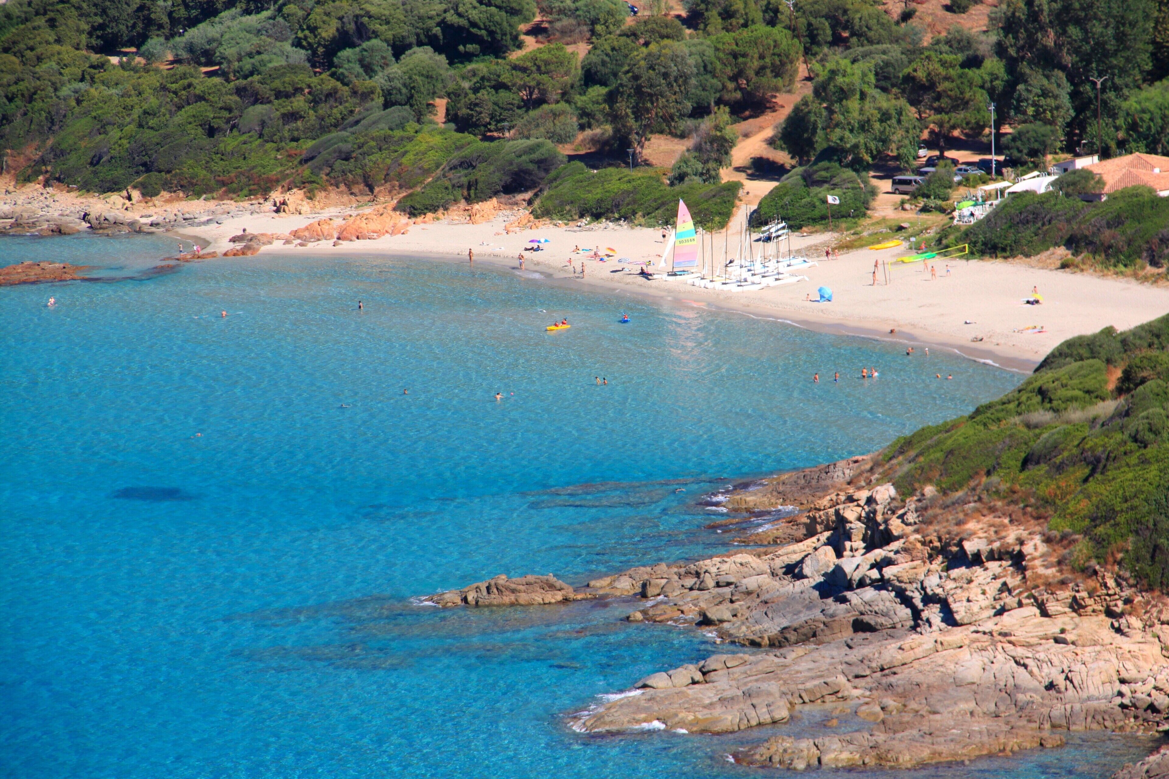 A coastal beach with clear blue waters, rocky shoreline, and a sandy beach area.