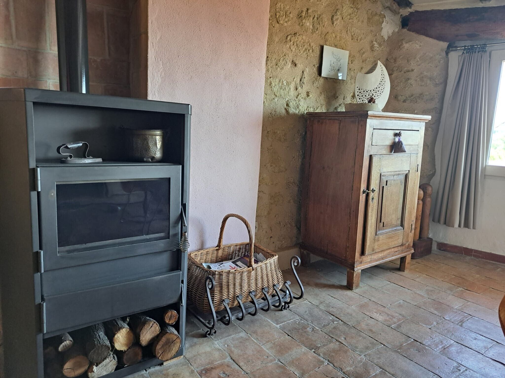 A rustic room with a wood-burning stove, a wicker basket, and a wooden cabinet.