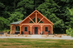 A wooden cabin with a triangular roof, a porch with seating, and a gravel driveway.