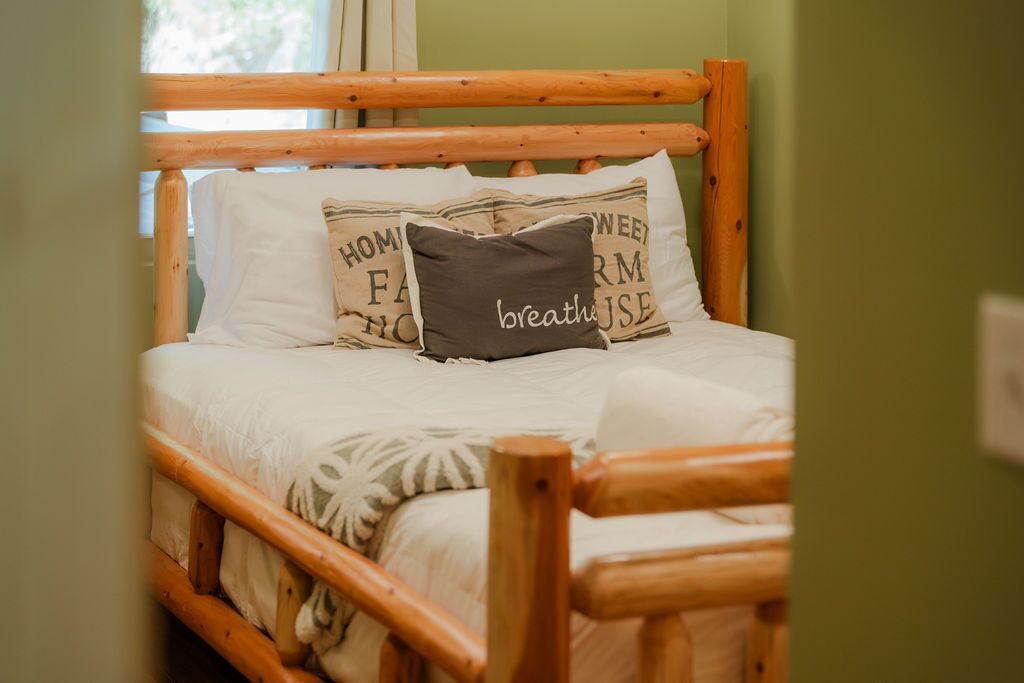 Una cama de madera con cabecera, ropa de cama blanca y almohadones decorativos con texto.