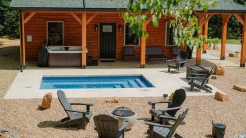 A wooden cabin with a hot tub, outdoor seating, and a swimming pool.