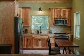 A kitchen with wooden cabinets, a refrigerator, a microwave, a stove, and a window.