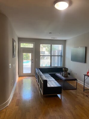 A spacious living area with hardwood flooring, a built-in bench, a flat-screen TV, and a large window with blinds. - Private 1-bedroom Apt with AC in amazing Atlanta. Near Mercedes-Benz Stadium!! (Atlanta)