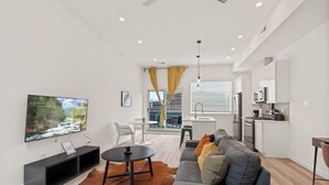 Ett modernt vardagsrum med en platt-TV, en soffa, ett soffbord och en matplats med ett litet bord och stolar.