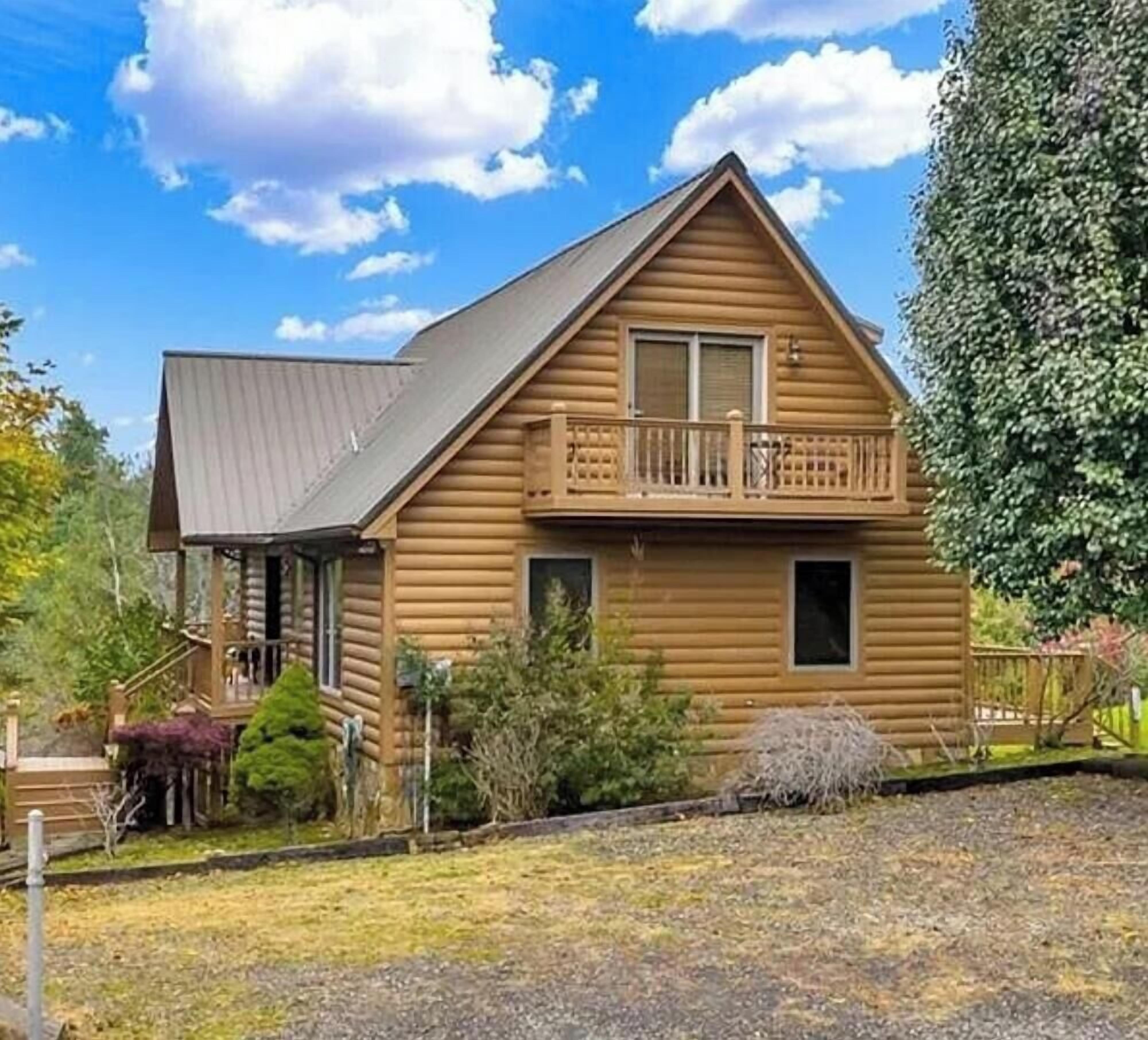 A two-story log cabin with a balcony, surrounded by a well-maintained yard.
