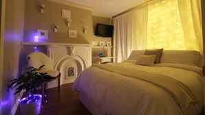 Ein Schlafzimmer mit einem großen Bett, einem flachbildfernseher an der Wand, einem Kamin und einem kleinen Tisch mit einem Laptop.