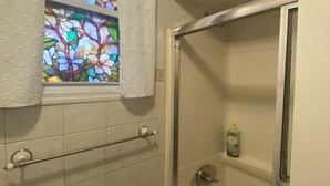 Ein Badezimmer mit Dusche, Handtuchhalter, einer Duschkabinentür aus Glas, einem Fenster mit Buntglasdekor und einer Seifenspenderflasche an der Wand.