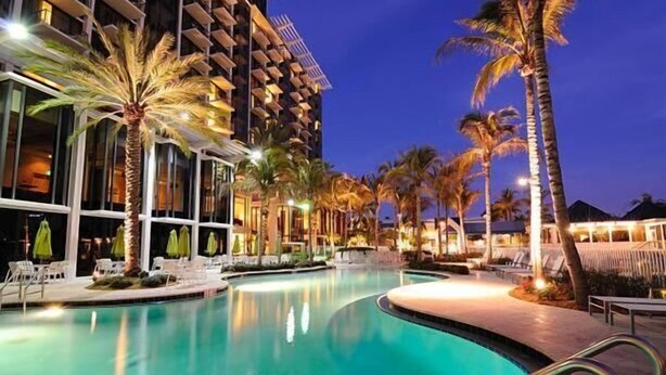 A hotel pool area with a curved pool, palm trees, and a building with balconies. - Toma Palace (Khelvachauri)