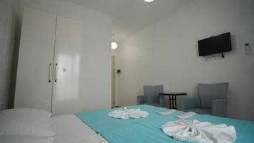 Quarto de hotel com uma cama, duas poltronas, uma mesa pequena, uma televisão e um guarda-roupa.