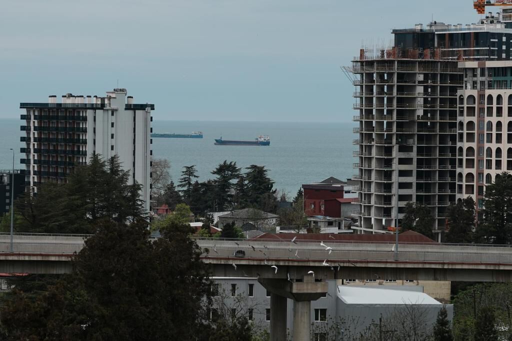 Un paisaje urbano costero con un puente, edificios y barcos a lo lejos.