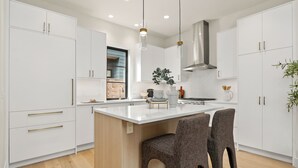 A modern kitchen with white cabinetry, a central island, two bar stools, pendant lighting, and a stainless steel range hood. - Bright + Modern DADU near Downtown Kirkland - Garage/EV +Private yard (Kirkland)