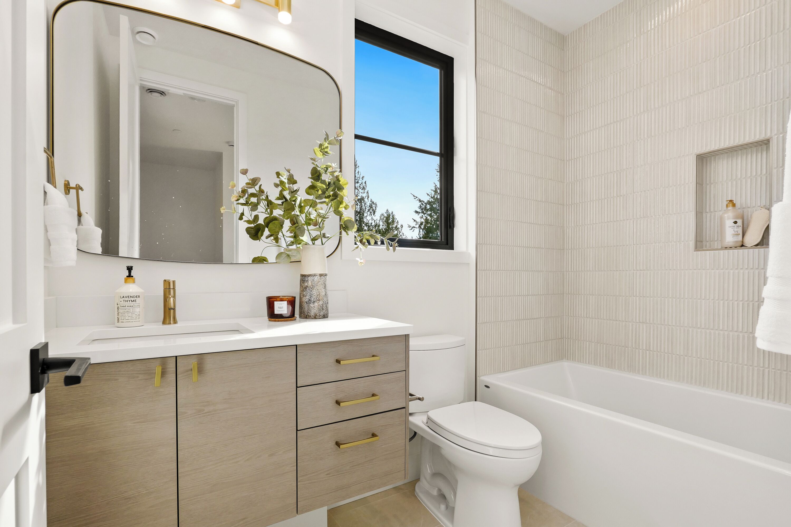 A modern bathroom with a white sink, a large mirror, a toilet, and a bathtub.