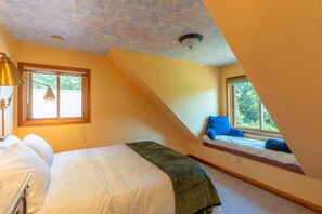 A bedroom with a bed, a desk, a chair, and a window with a view of trees. - Whitefish Mountain Farmhouse | Near Glacier (Whitefish)