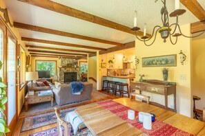 A cozy living room with a fireplace, wooden beams, a dining area with a red rug, and a kitchen with a brick backsplash. - Whitefish Mountain Farmhouse | Near Glacier (Whitefish)
