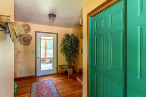 A hallway with a wooden floor, a green door, a potted plant, a bench, and a rug. - Whitefish Mountain Farmhouse | Near Glacier (Whitefish)