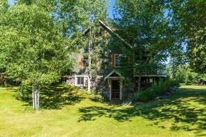 A stone house with a wooden porch, surrounded by lush greenery and trees. - Whitefish Mountain Farmhouse | Near Glacier (Whitefish)