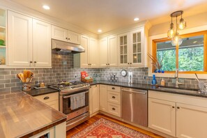 A modern kitchen with white cabinets, a stainless steel stove, and a window with a view of trees. - Whitefish Mountain Farmhouse | Near Glacier (Whitefish)
