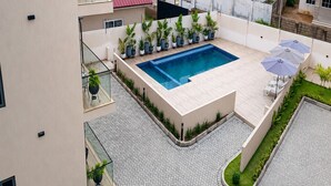 Una piscina en la azotea con plantas en macetas, una zona de estar con sombrillas y un patio empedrado.