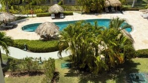 Um resort com piscina, palmeiras e um edifício com varandas.