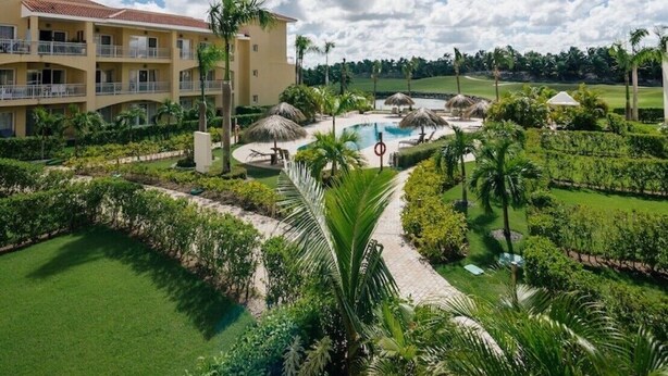 Um resort com piscina, palmeiras e um campo de golfe ao fundo.