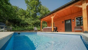 A wooden cabin with a swimming pool, outdoor seating, and a grill area.