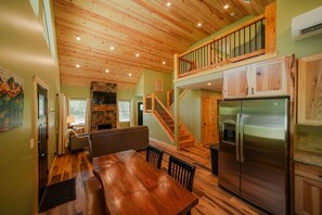 A spacious kitchen with a wooden ceiling, a dining area with a wooden table and chairs, a built-in oven, and a refrigerator.