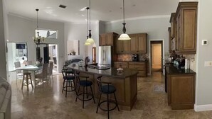 Cozinha ampla com uma ilha grande, banquetas, armários de madeira e iluminação pendente.