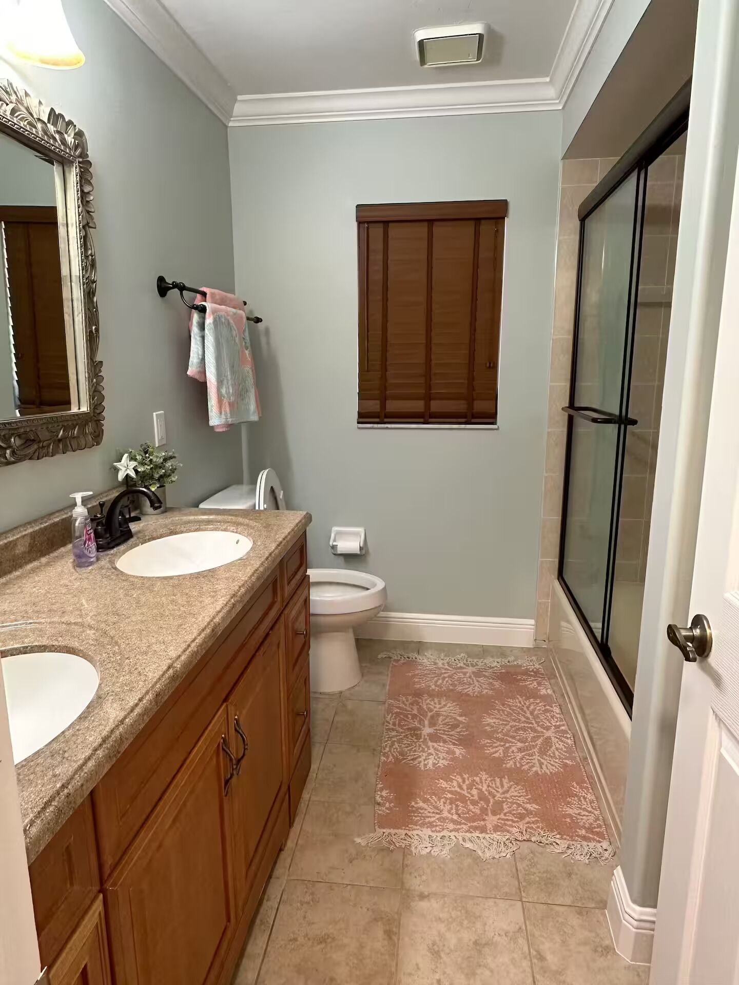 A bathroom with two sinks, a toilet, a shower, a large mirror, and a window with blinds.