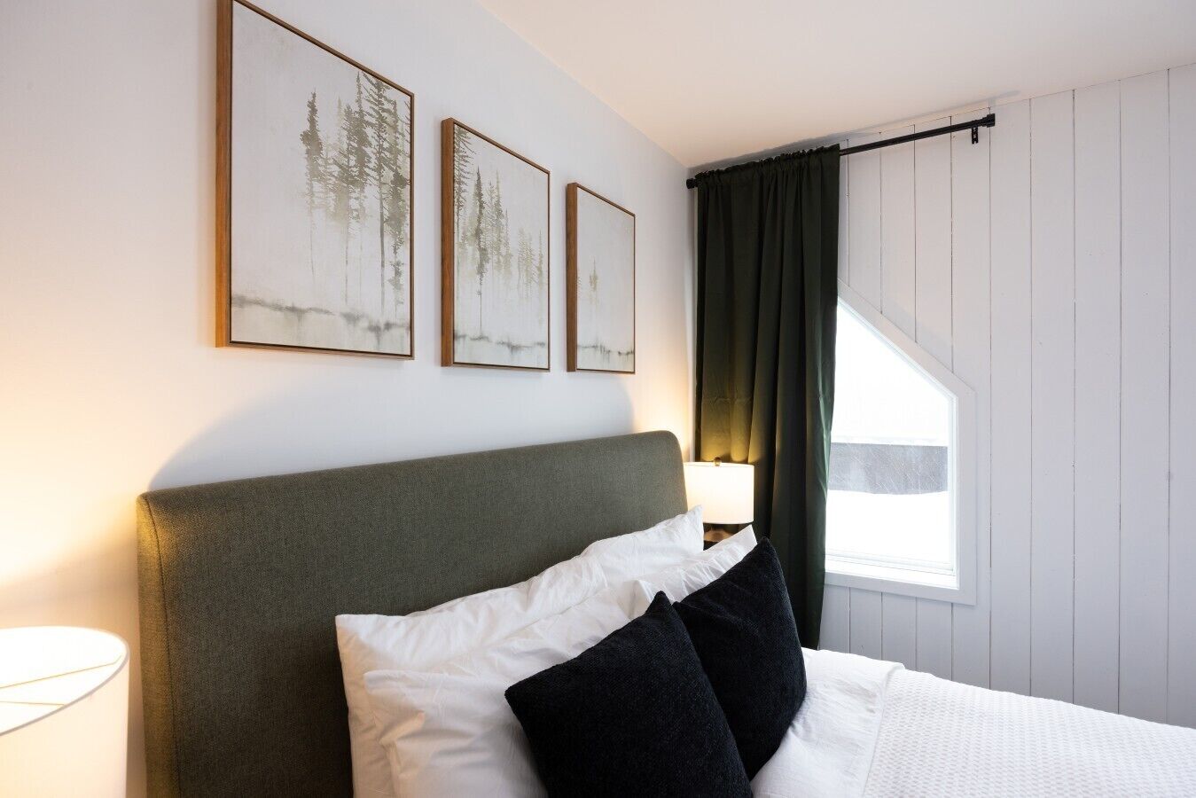 A hotel room with a bed, a nightstand with a lamp, and three framed pictures on the wall.