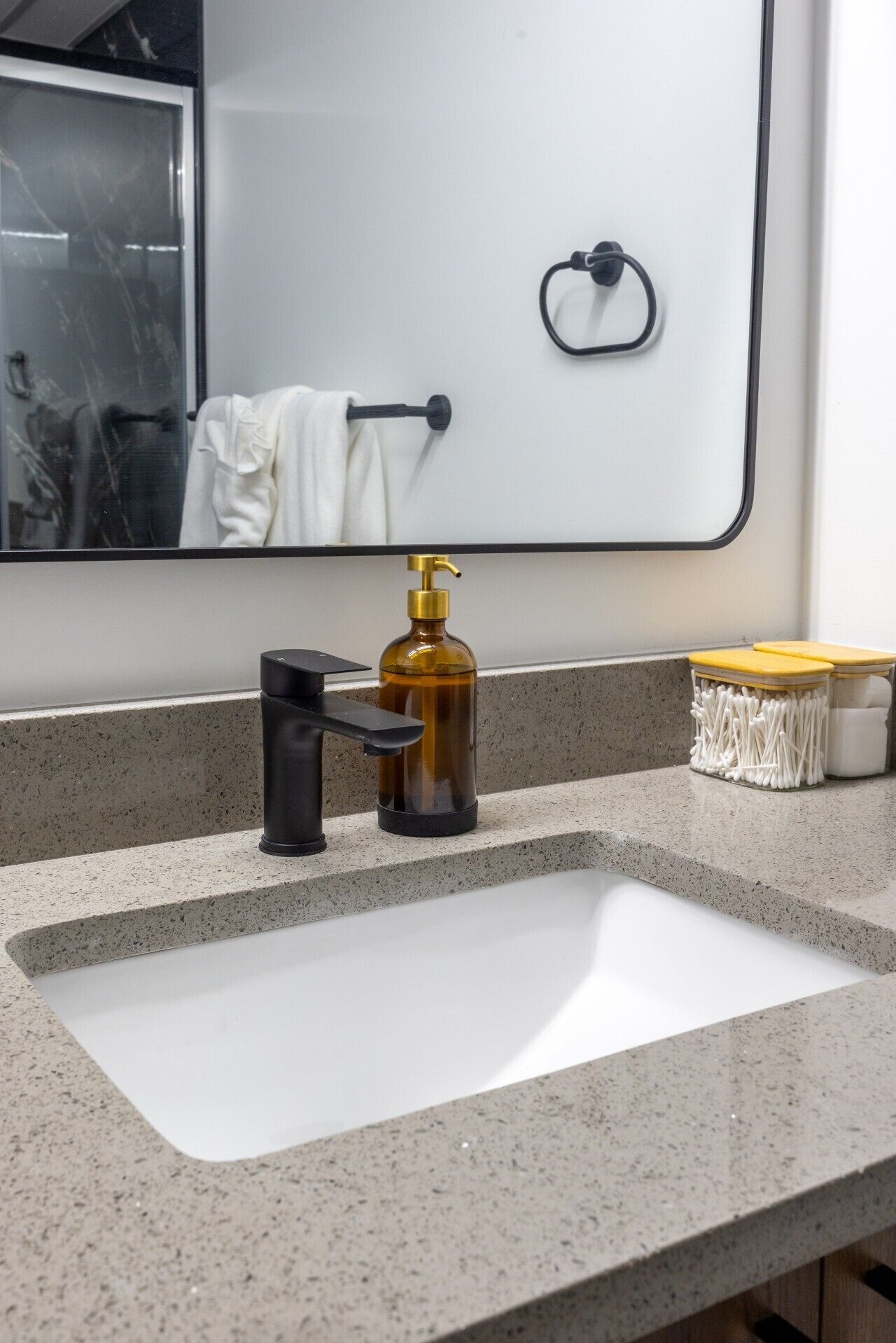 A bathroom with a white sink, a black faucet, a gold soap dispenser, and a mirror above the sink.
