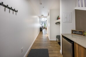 A hallway with a wooden floor, a kitchen area with a dishwasher, and a sign that reads 'gather with grateful hearts'.
