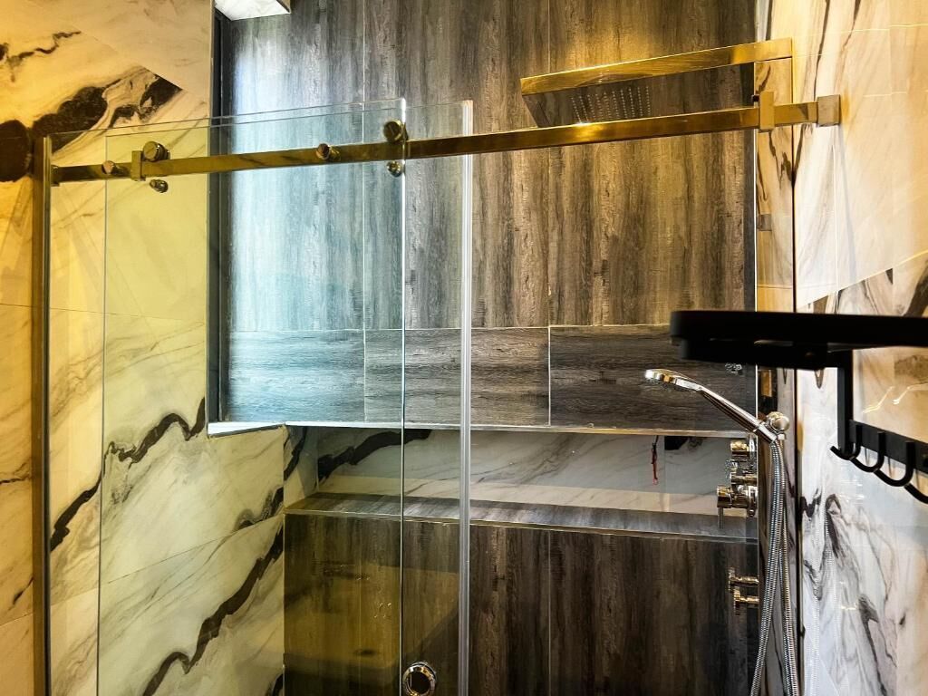 A modern bathroom with a glass shower enclosure, marble walls, and a wooden floor.