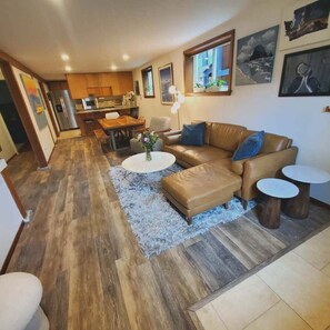 A modern living room with a brown leather sofa, a coffee table, and a dining area with wooden furniture. - The Holdfast: Rare 3-Bedroom Garden Retreat Near Old Ballard (Seattle)