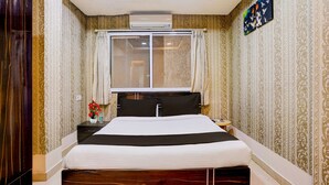Ein Hotelzimmer mit einem Bett, einem Fenster, einem Nachttisch und einer Wand-Klimaanlage.