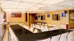 Ein Konferenzraum mit langem Tisch und weißen Stühlen, einem Deckenventilator und einem Fenster mit Vorhängen.