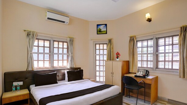 Ein Hotelzimmer mit Bett, Schreibtisch, Stuhl und zwei mit Vorhängen versehenen Fenstern.