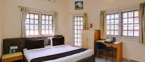 Habitación de hotel con cama, escritorio, silla y dos ventanas con cortinas.