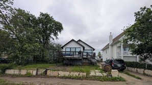 A residential area with two houses, one with a deck and a garage, and a driveway with a car parked.