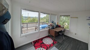 A room with a desk, a chair, a window with blinds, a door, and a view of the outdoors.