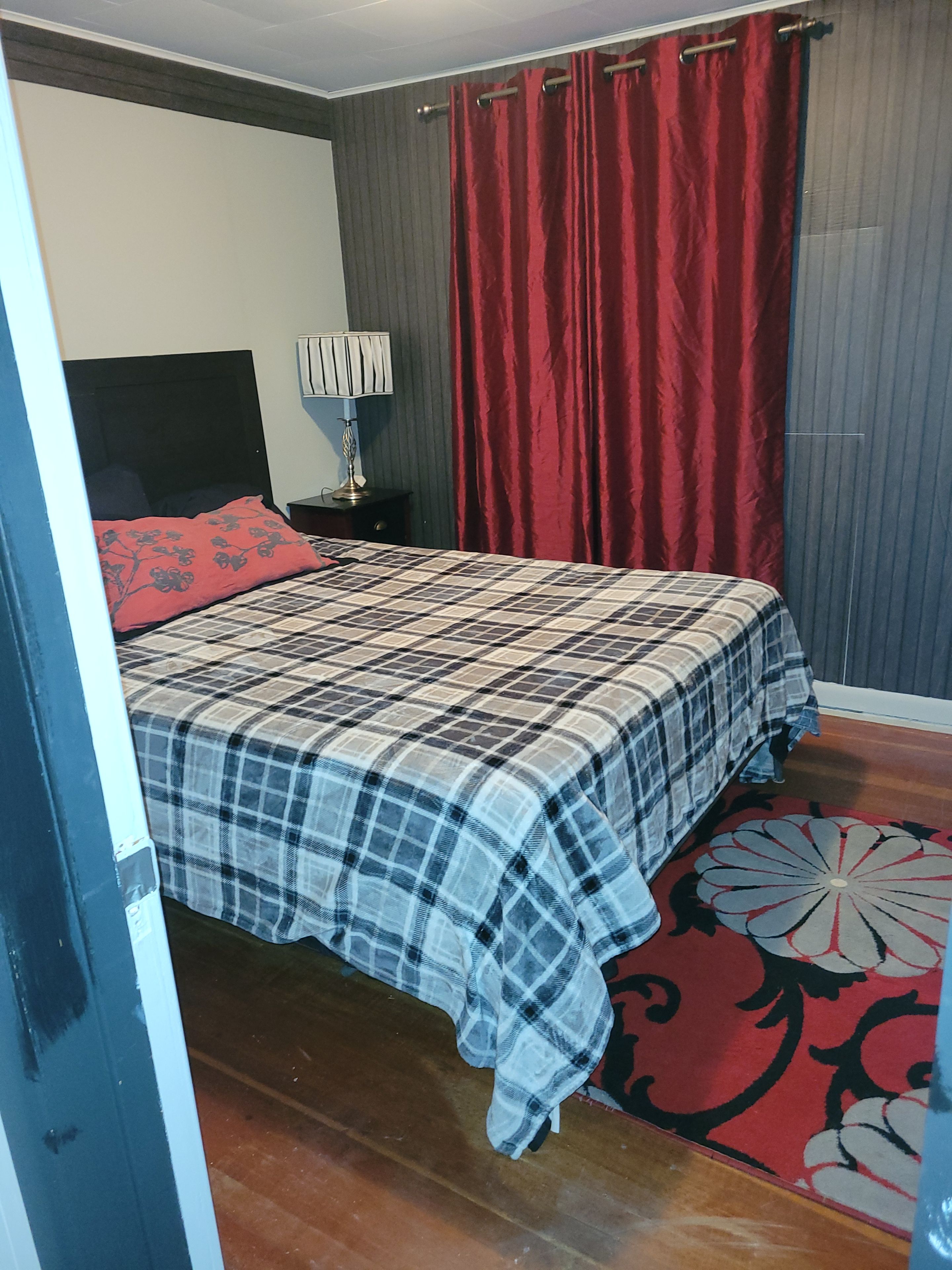 Une chambre à coucher avec un lit, une table de chevet, une lampe, un rideau rouge et un tapis à motifs.