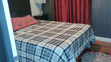 Une chambre à coucher avec un lit, une table de chevet, une lampe, un rideau rouge et un tapis à motifs.
