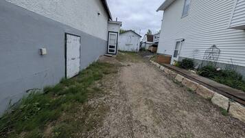 A narrow gravel path between two white buildings with a metal gate and a small air conditioning unit.