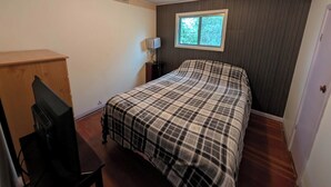 A bedroom with a bed, a dresser, a desk, a lamp, and a window.