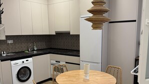 A modern kitchen with white cabinets, a washing machine, a sink, and a round dining table with wicker chairs. - Guipuzcua  (Pamplona)