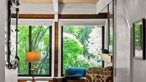 Una habitación con techo de madera, ventanas amplias, un sillón estampado, un sofá y una lámpara.