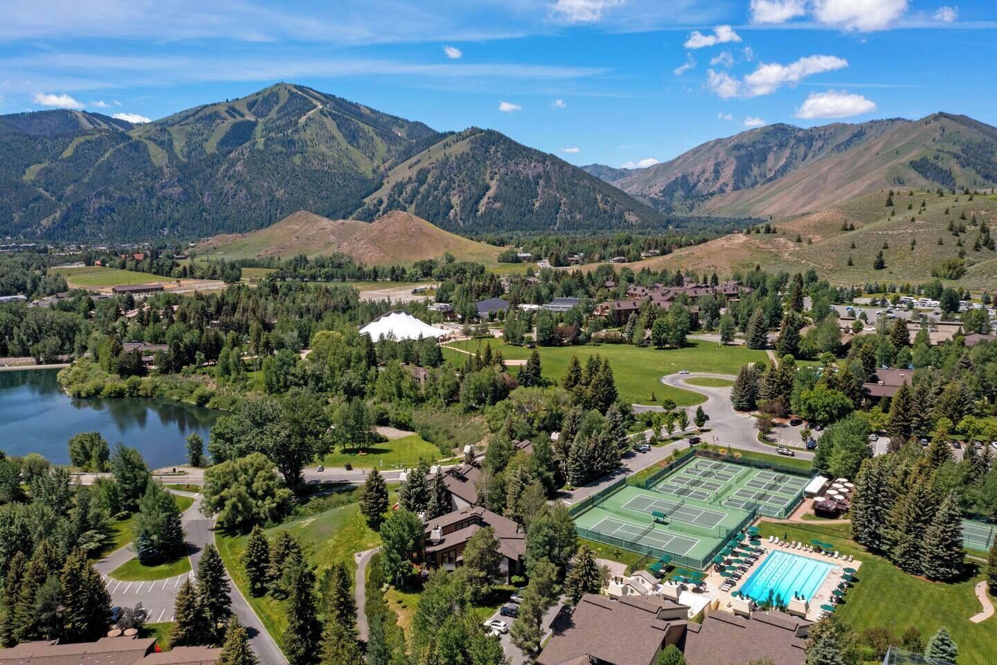 Un quartier résidentiel avec un lac, des courts de tennis et des montagnes en arrière-plan.