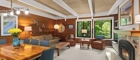A modern living room with a wooden ceiling, a fireplace, a dining area, and large windows.