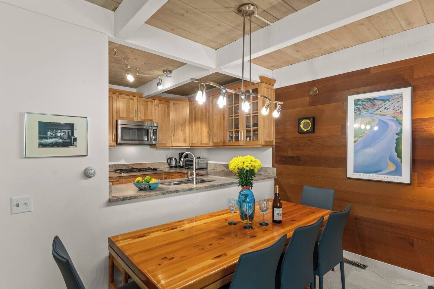 A modern kitchen with wooden cabinets, a stainless steel microwave, and a dining area with a wooden table and chairs.