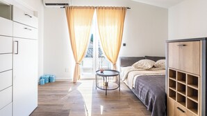 Un dormitorio con cama, armario, una mesita redonda y vistas a través de cortinas.