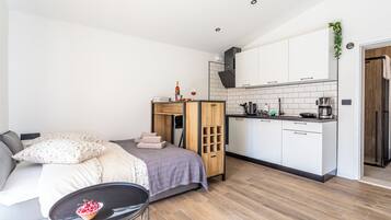 Ein kompakter Wohnraum mit Küchenzeile, einem Bett mit Kopfteil, einem kleinen Esstisch und einer Topfpflanze.
